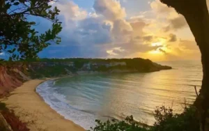 Praia de Juacema na Bahia ao pôr do sol, vista aérea com falésias e mar calmo.