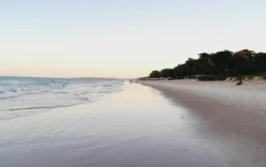 Praia do Mundaí em Porto Seguro ao entardecer, com faixa de areia larga e mar calmo refletindo o céu.