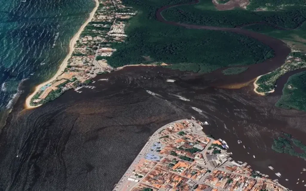 Vista aérea da balsa Arraial d'Ajuda atravessando o rio Buranhém, conectando Porto Seguro e Arraial d'Ajuda, com embarcações visíveis.