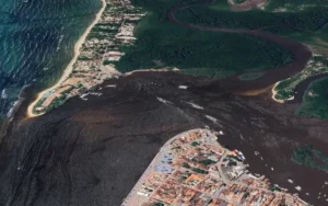 Vista aérea da balsa Arraial d'Ajuda atravessando o rio Buranhém, conectando Porto Seguro e Arraial d'Ajuda, com embarcações visíveis.