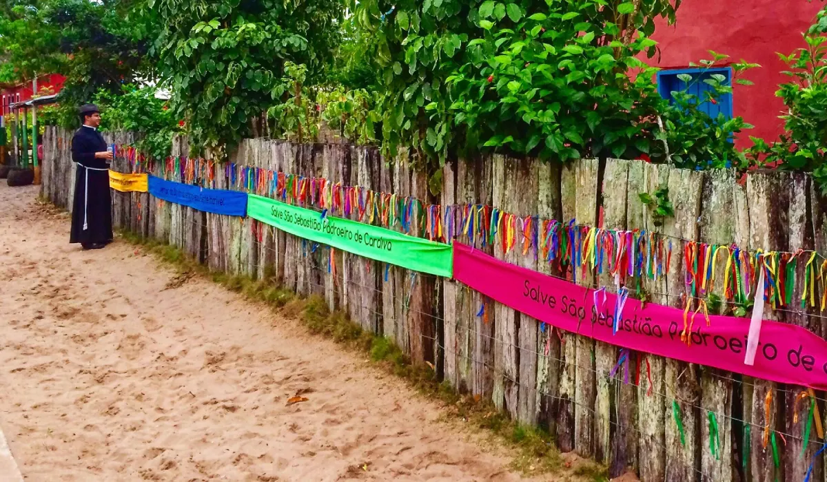 Em Caraíva, onde a rua é feita de areia e o tempo corre devagar, a fé se manifesta em cores vibrantes. A cerca rústica, adornada com fitas de pedidos e faixas de celebração a São Sebastião, o padroeiro de Caraíva, cria um cenário único de tradição e cultura. Uma imagem que captura a alma simples e acolhedora deste vilarejo mágico na Bahia.