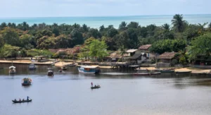 Vista panorâmica da travessia do Rio Caraíva com pequenos barcos e canoas, mostrando o acesso final à vila rústica e as casas coloridas na margem oposta. Imagem ilustra a chegada do trajeto Porto Seguro para Caraíva.