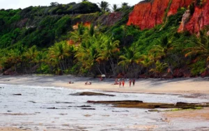 Praia de Pitinga em Arraial d'Ajuda com falésias coloridas, coqueiros, areia clara e mar azul-esverdeado.