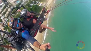 Voo de paramotor em Porto Seguro sobre a praia de Taperapuã, mostrando um piloto e passageiro sorrindo com a vista aérea da Orla Norte.