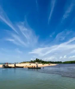 Praia de Caraíva com o encontro do rio e o mar, barcos na areia e céu azul.
