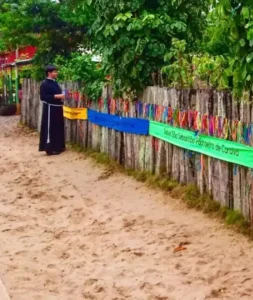Festa de São Sebastião em Caraíva, com padre, cerca de madeira e fitinhas coloridas, representando os eventos de Porto Seguro e região.