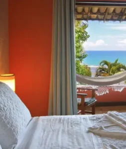 Quarto de hotel com vista para o mar e rede na varanda, promovendo hospedagens em Porto Seguro e região.
