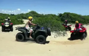 Grupo fazendo passeio de quadriciclo em Trancoso, Bahia, em trilha de areia entre a vegetação da restinga.