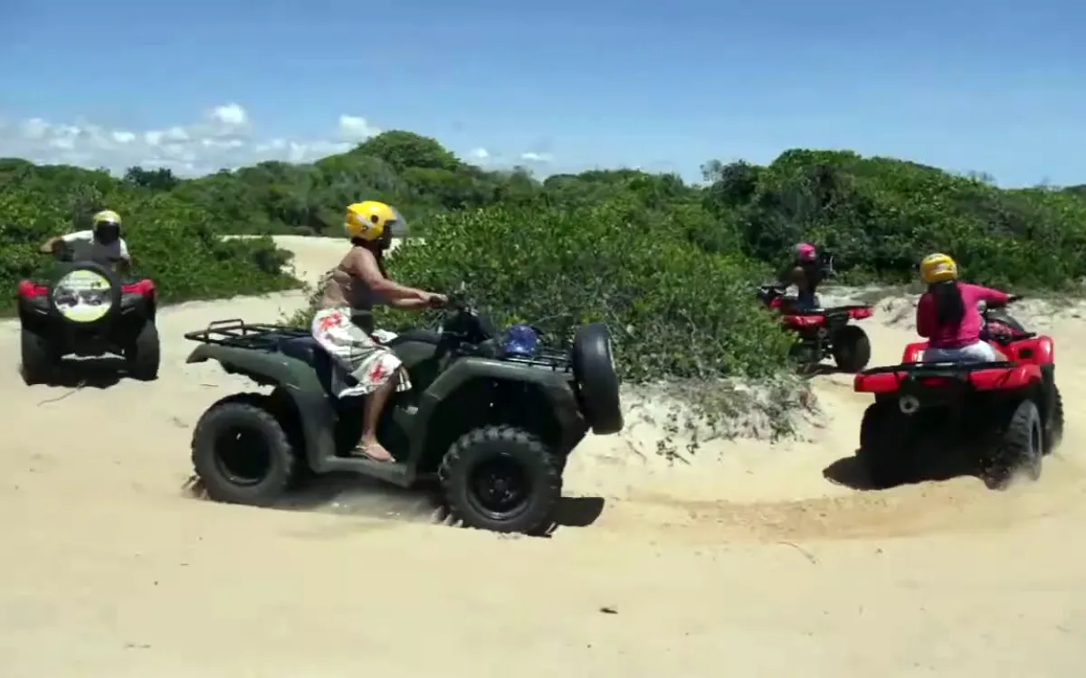Grupo fazendo passeio de quadriciclo em Trancoso, Bahia, em trilha de areia entre a vegetação da restinga.