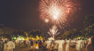 Fogos de artifício iluminam o céu sobre o Quadrado de Trancoso durante a festa de Réveillon, com pessoas vestidas de branco celebrando. Réveillon em Trancoso: Guia para a Festa.