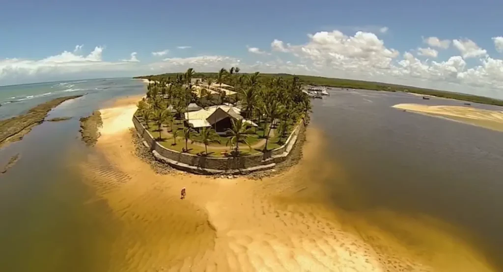 Vista aérea do Arraial Eco Resort na Ponta do Apaga-Fogo em Arraial d'Ajuda, destacando as piscinas, a praia privativa e o encontro do rio com o mar em Porto Seguro.