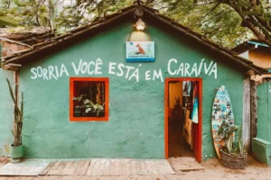 Fachada de casa rústica verde em Caraíva com a frase "Sorria você está em Caraíva" escrita na parede e uma prancha de surf decorativa na entrada.