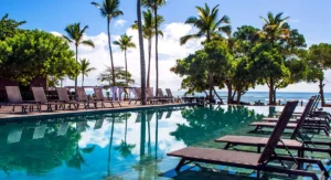 Piscina de borda infinita do Kuara Hotel refletindo o céu e coqueiros, com espreguiçadeiras modernas e vista para o mar da Praia da Pitinga em Arraial d'Ajuda.