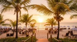 Vista da praia do La Torre Resort em Porto Seguro durante o nascer do sol, com guarda-sóis brancos na areia e coqueiros em primeiro plano.