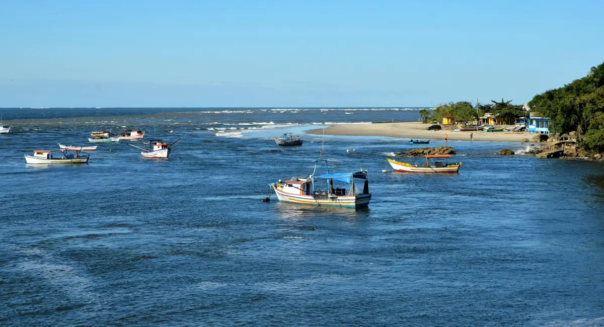 Barcos de pesca coloridos navegando na foz do rio em Caraíva, Bahia, sob um céu azul limpo — destino comum de transfer saindo do Aeroporto de Porto Seguro.
