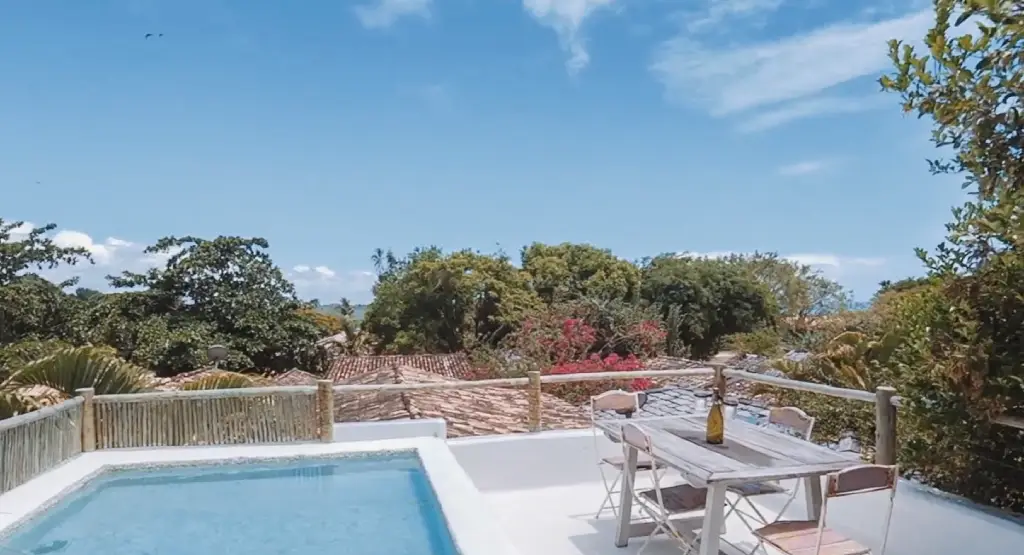 Terraço privativo do UXUA Casa Hotel & Spa em Trancoso com pequena piscina de hidromassagem, mesa de madeira e vista para os telhados rústicos e vegetação nativa.