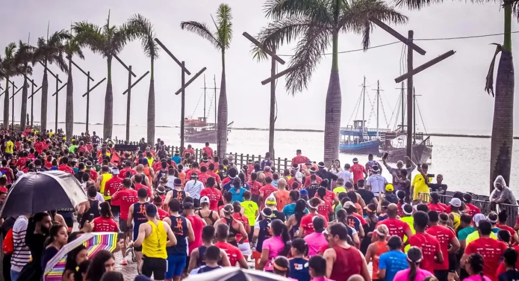 Multidão de corredores com camisas vermelhas e rosas na Nova Passarela da Cultura em Porto Seguro durante a Meia Maratona do Descobrimento.