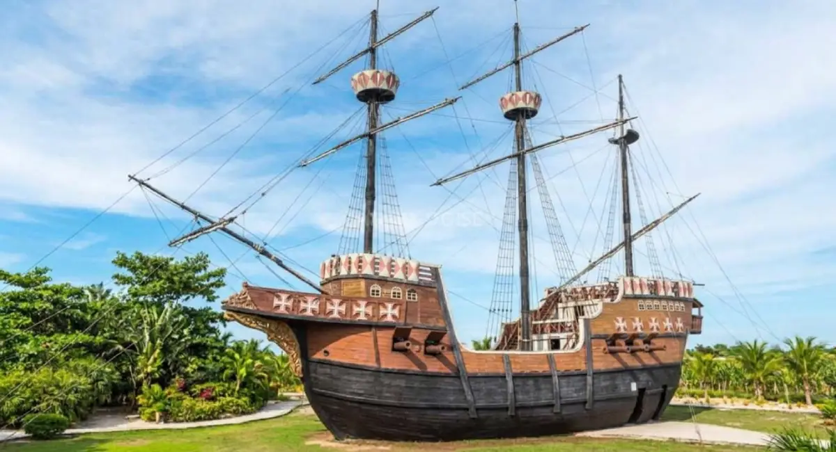 Réplica em tamanho real da caravela portuguesa Nau Capitânia de Pedro Álvares Cabral, exibida em uma área gramada no Memorial da Epopeia do Descobrimento em Porto Seguro, Bahia. O navio histórico de madeira possui mastros altos, cordas e detalhes da época colonial sob um céu azul claro.